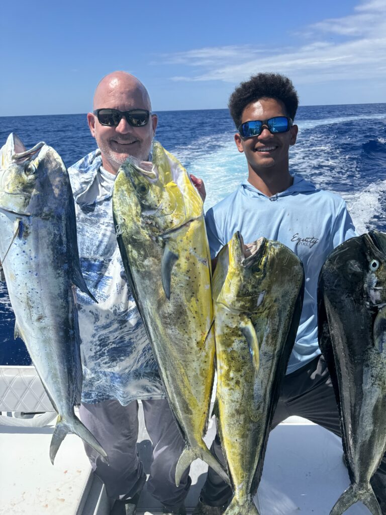 two smiling people on a boat hold up large fish